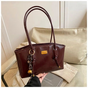 Detail of dark burgundy glossy faux leather bag with gold logo plate and tassel