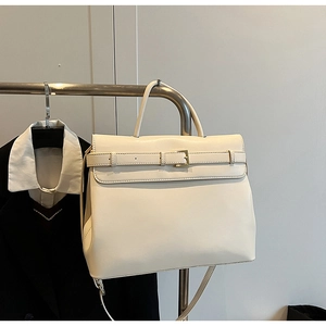 Detailed view of cream white trapezoid handbag hanging on a metal display stand
