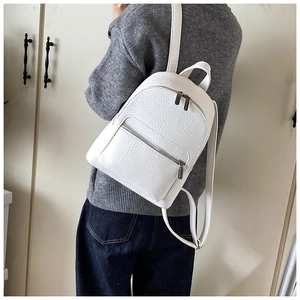 Back view of a white lychee grain leather backpack worn over a grey sweater in a home setting