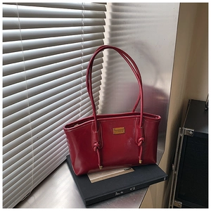 Detail of red glossy patent leather tote bag featuring a decorative knot and gold logo plate
