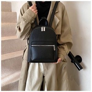 Close-up of a black lychee texture leather backpack with silver zippers worn by a model