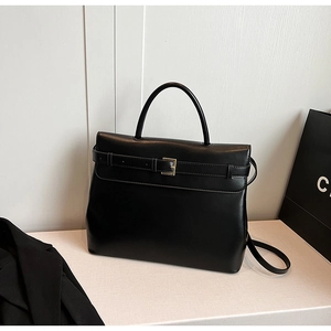 Detailed view of black matte leather trapezoid handbag with decorative buckle and strap