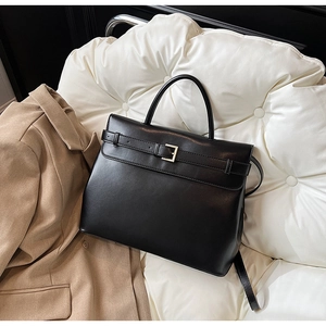 Close-up of black matte leather handbag with gold buckle detail and sleek shoulder strap