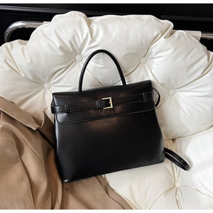 Close-up of black leather briefcase with gold metal buckle on a white quilted cushion