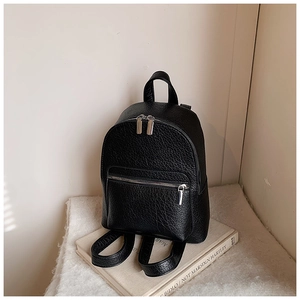 Detail of black pebble leather backpack with silver zippers and top handle on a book