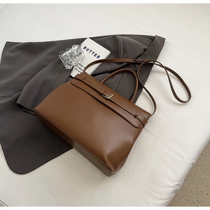 Detail of a brown leather briefcase bag featuring a stylish metal buckle and top handles
