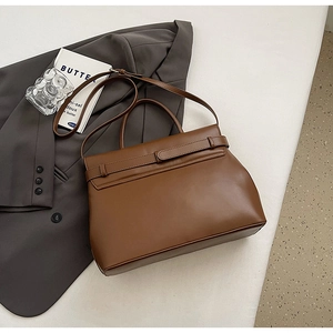Brown leather trapezoid handbag placed on a grey blazer with artistic decoration
