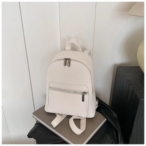 Detail of cream-white pebble grain backpack featuring silver zippers and front pocket
