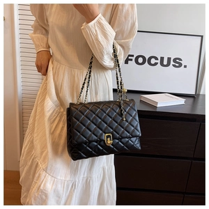 Detail of a black quilted chain bag with gold twist lock and woven leather strap
