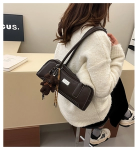 Detail of dark brown leather cylindrical bag with white contrast stitching and plush bear