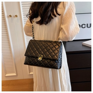 Close-up of black quilted leather crossbody bag with golden chain and square lock