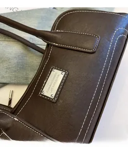 Detail of dark brown leather shoulder bag featuring white contrast stitching and silver plaque