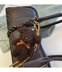 Detailed view of a brown plush bear charm with a satin bow on a leather shoulder bag