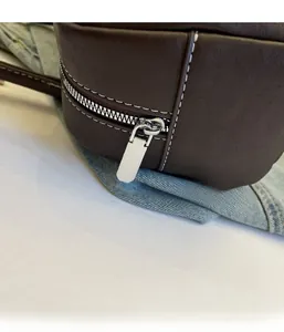 Detailed view of silver metal zipper and white stitching on vintage brown leather handbag