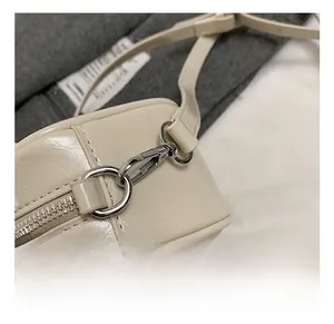 Detailed macro view of silver metal swivel hook and glossy off-white patent leather bag
