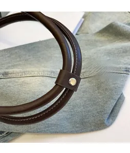 Detail of brown leather handles with contrast stitching and silver metal snaps on a handbag