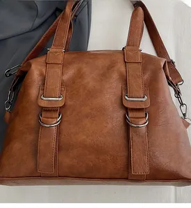 Detailed close-up of brown textured leather tote bag with silver metal rings and buckles