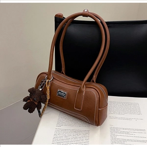 Detailed close-up of a vintage brown leather bag with white contrast stitching and bear charm