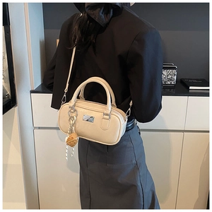 Chic cream-colored bowling bag with heart charm shown as a crossbody on a model