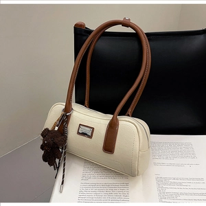 Close-up of cream cylinder bag with brown handles and a dark brown plush charm