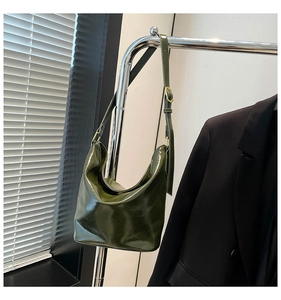 Detail of dark green glossy shoulder bag featuring wrinkled texture and adjustable gold buckle