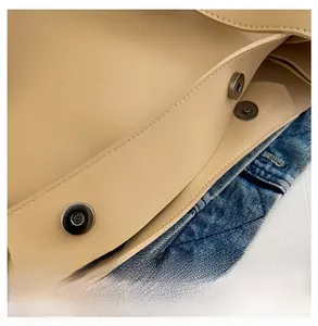 Close-up of silver magnetic clasp on beige leather shoulder bag with precision stitching