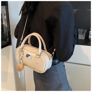 Detail of cream bowling bag showing smooth leather texture and metal logo plaque