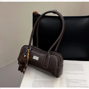 Detail of vintage brown shoulder bag with contrast stitching and teddy bear charm