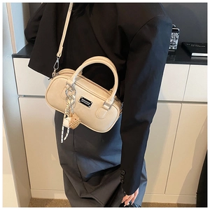 Detail of a cream bowling handbag with adjustable strap and baseball charm on a model