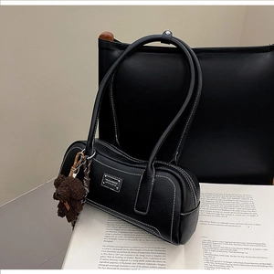 Detail of black faux leather bag with contrast stitching and a teddy bear charm