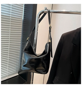 Detail of glossy black oil-wax leather shoulder bag with sleek adjustable golden buckles
