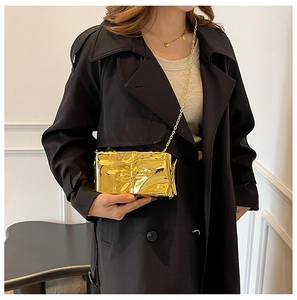 Detalle de bolso de noche plisado dorado metalizado con cadena sobre abrigo negro