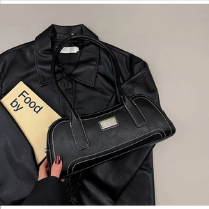 Detail of black leather underarm bag with white contrast stitching and silver metal logo
