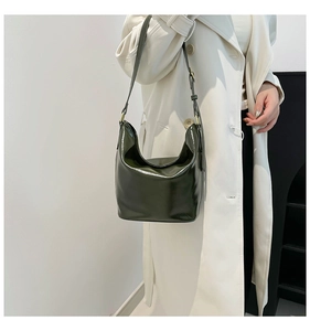 Detail of a dark green hobo bag in glossy leather worn by a model in a trench coat