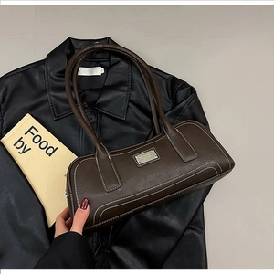 Macro detail of dark brown leather bag with white contrast stitching and metal logo