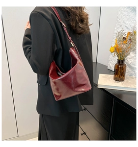 Detailed close-up of a burgundy patent leather half-moon shoulder bag on a model