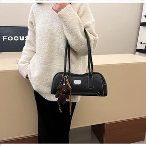 Detail of black faux leather shoulder bag with white contrast stitching and bear charm