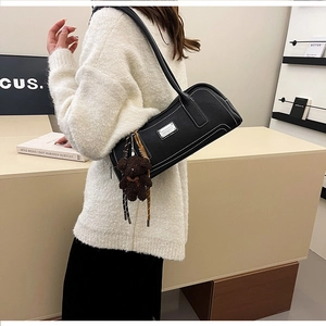 Detail of black pebbled leather baguette bag with white stitching and bear charm on model