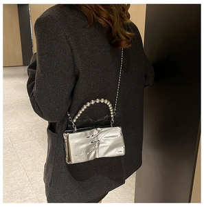 Detalle de bolso plateado metalizado con asa de cuentas y correa de cadena al hombro
