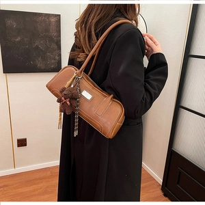 Detail of vintage brown leather baguette bag with white stitching and bear charm