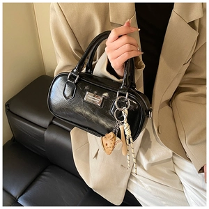 Detail of black glossy boston bag featuring metallic logo and baseball charms on leather