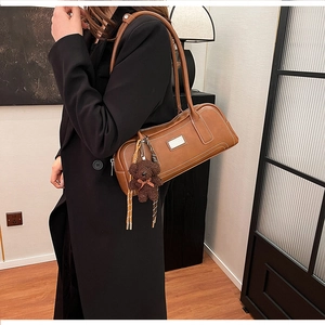 Detail of vintage brown shoulder bag with plush bear charm worn on a black wool coat