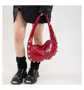 Detail of red patent leather crescent bag with silver studs held by model in black outfit