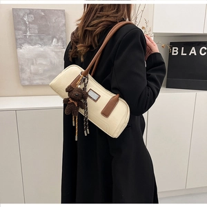 Detail of a creamy white cylindrical shoulder bag with brown leather straps and bear charm