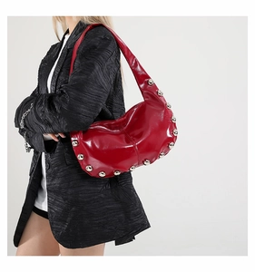Detail of red crescent shoulder bag with glossy finish and large silver metal rivets