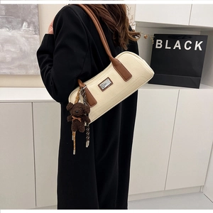 Detail of cream leather shoulder bag with brown handle and plush bear charm accessory