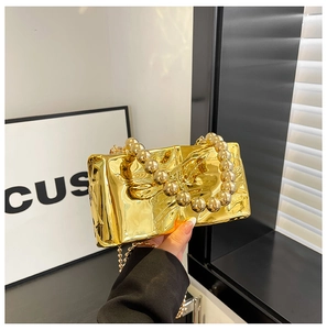 Detalle de bolso de noche de acrílico espejo dorado con asa de cuentas y cadena fina
