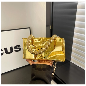Detalle de bolso de noche dorado efecto espejo con textura foil y asa de cuentas