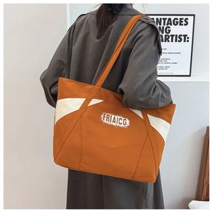 Detail of a large orange and beige canvas tote bag worn by a model in a modern room