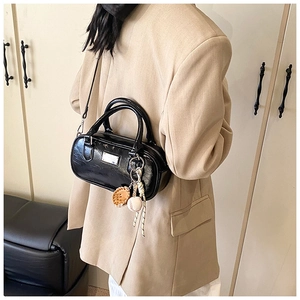 Detail of black glossy bowling bag with sports charm worn with an apricot suit jacket